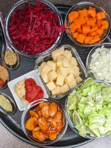 Vibrant vegetable ingredients arranged for a healthy vegetarian borscht recipe on a black tray.